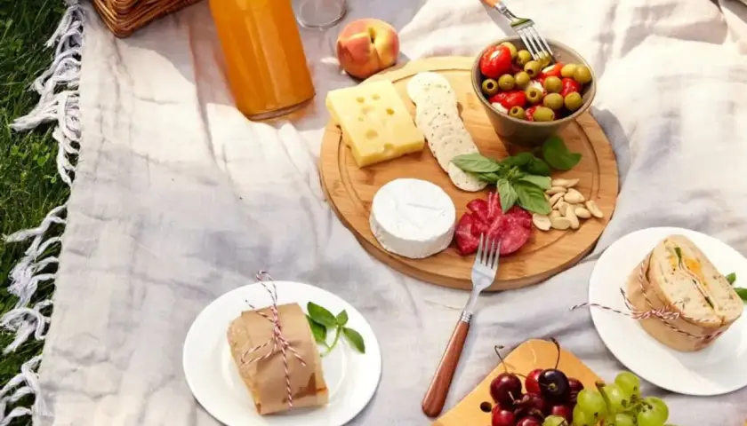 Idée de que prendre pour un picnic entre amis : plateau de fromages, charcuterie, olives, fruits, sandwichs et jus.