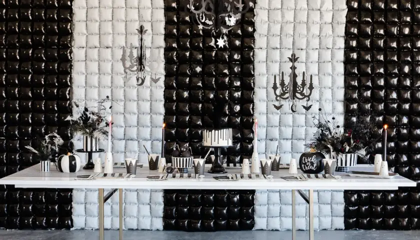 Table dressée pour une activité anniversaire mercredi Addams : gâteau, citrouille, décorations gothiques sur fond rayé noir et blanc.