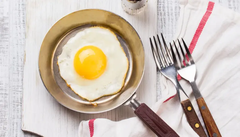 Un œuf au plat parfait, cuisiné dans une poêle inox, prêt à être dégusté avec deux fourchettes.