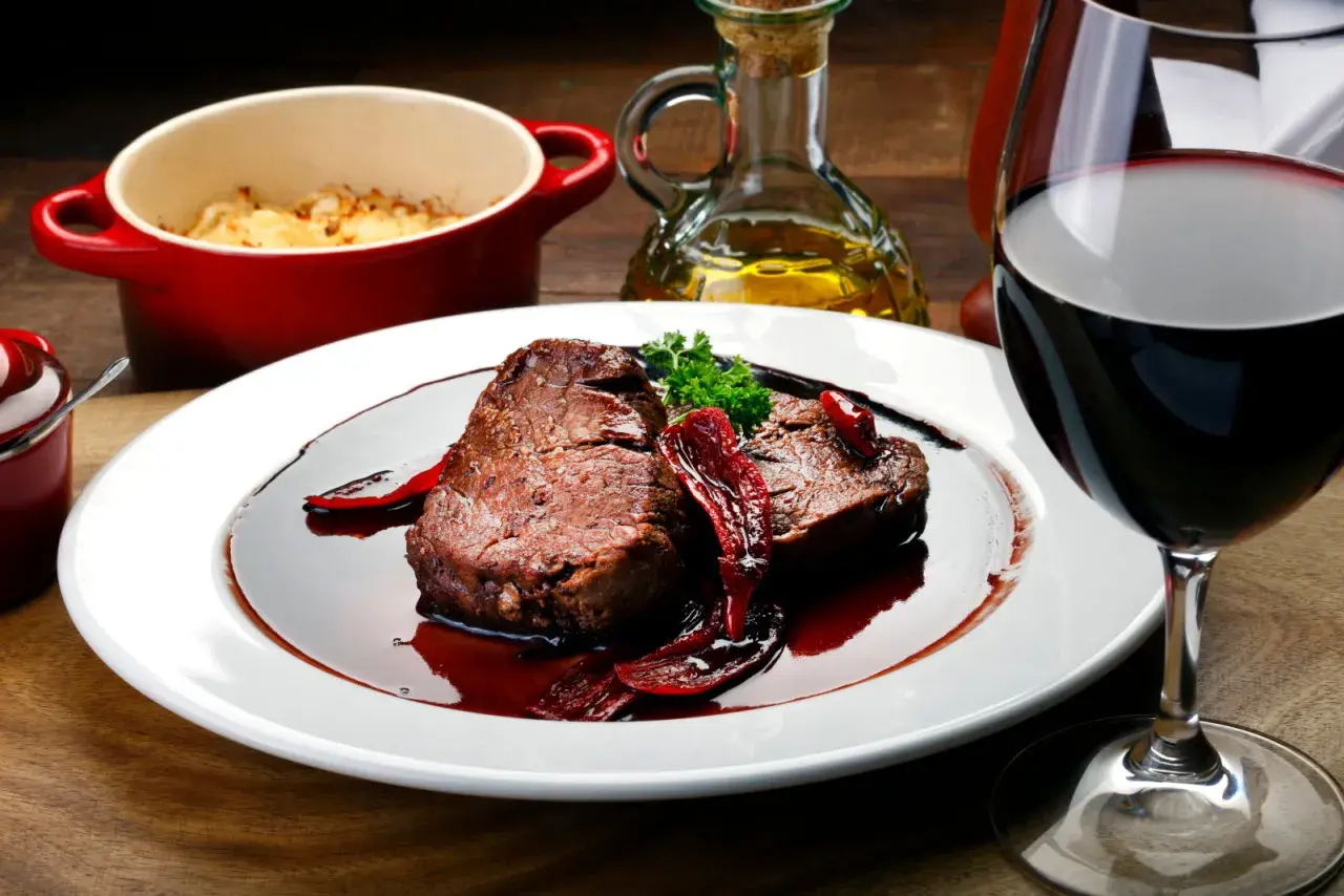 Un plat de viande rouge en sauce, accompagné d'une purée gratinée et d'un verre de vin. Parfait pour savoir que manger avec un sancerre rouge.
