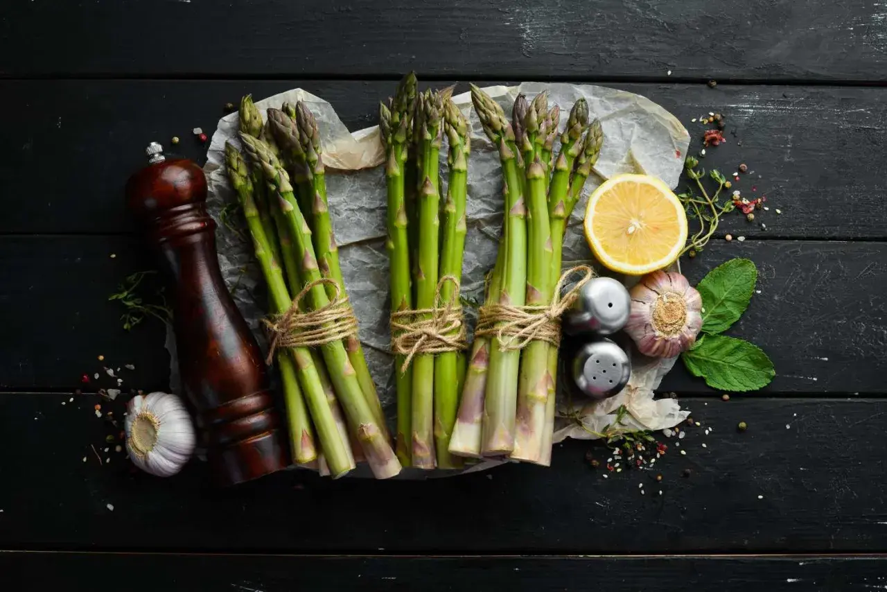 Des asperges fraîches, citron, ail et moulin à poivre sur fond noir. Idéal pour savoir quel vin avec asperges.