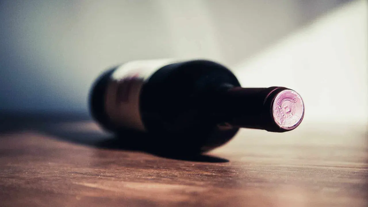 Une bouteille de vin couchée sur une table en bois. La question se pose : 1 bouteille de vin pour combien de personnes ?