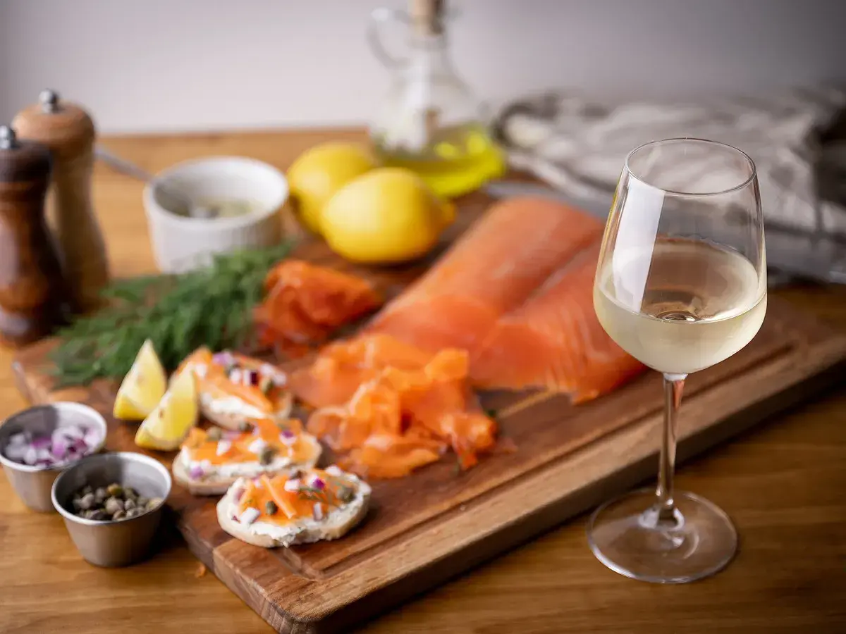 Un verre de vin blanc, parfait pour accompagner le saumon fumé, est présenté avec des toasts, des câpres, des oignons rouges et du citron.