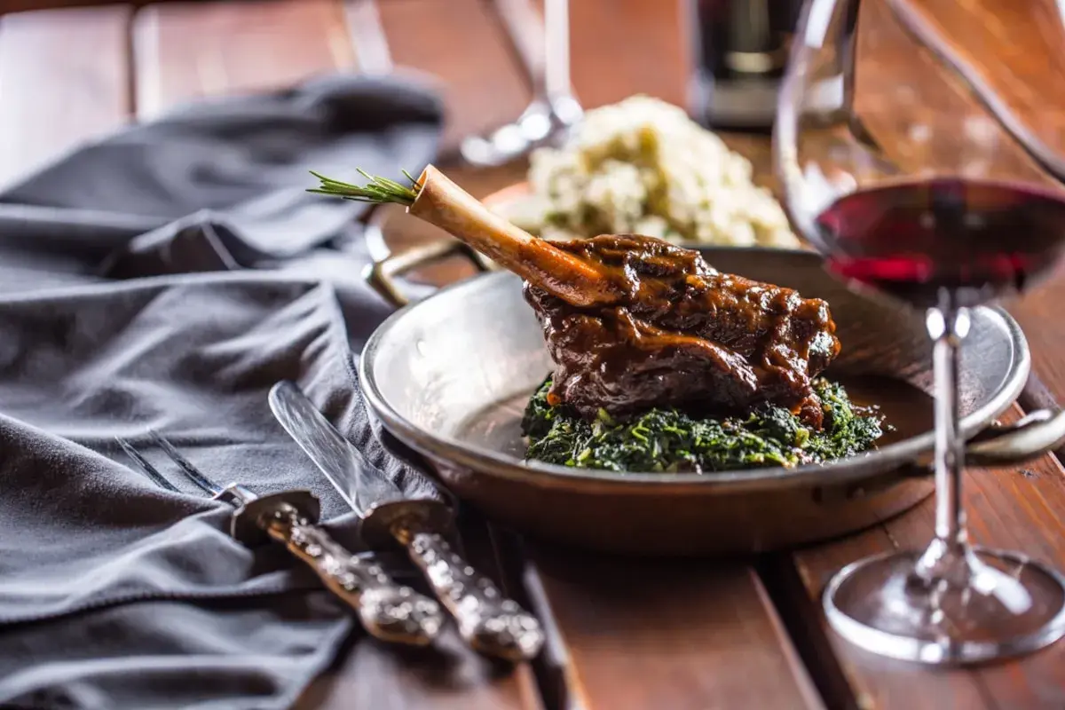 Un plat de vin avec agneau, servi sur un lit d'épinards, avec une branche de romarin. Un verre de vin rouge est à côté.