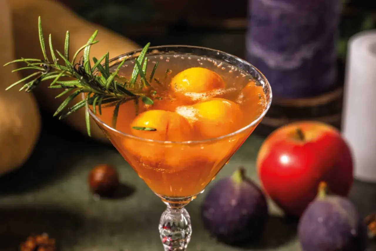 Cocktail fruité avec des pêches et du romarin, parfait pour une idée apéro mariage. Pomme et figues en arrière-plan.
