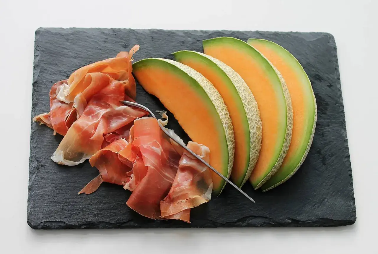 Tranche de melon et jambon cru sur ardoise. Quel vin avec melon et jambon cru ? Un vin blanc sec et fruité ou un rosé léger serait parfait.