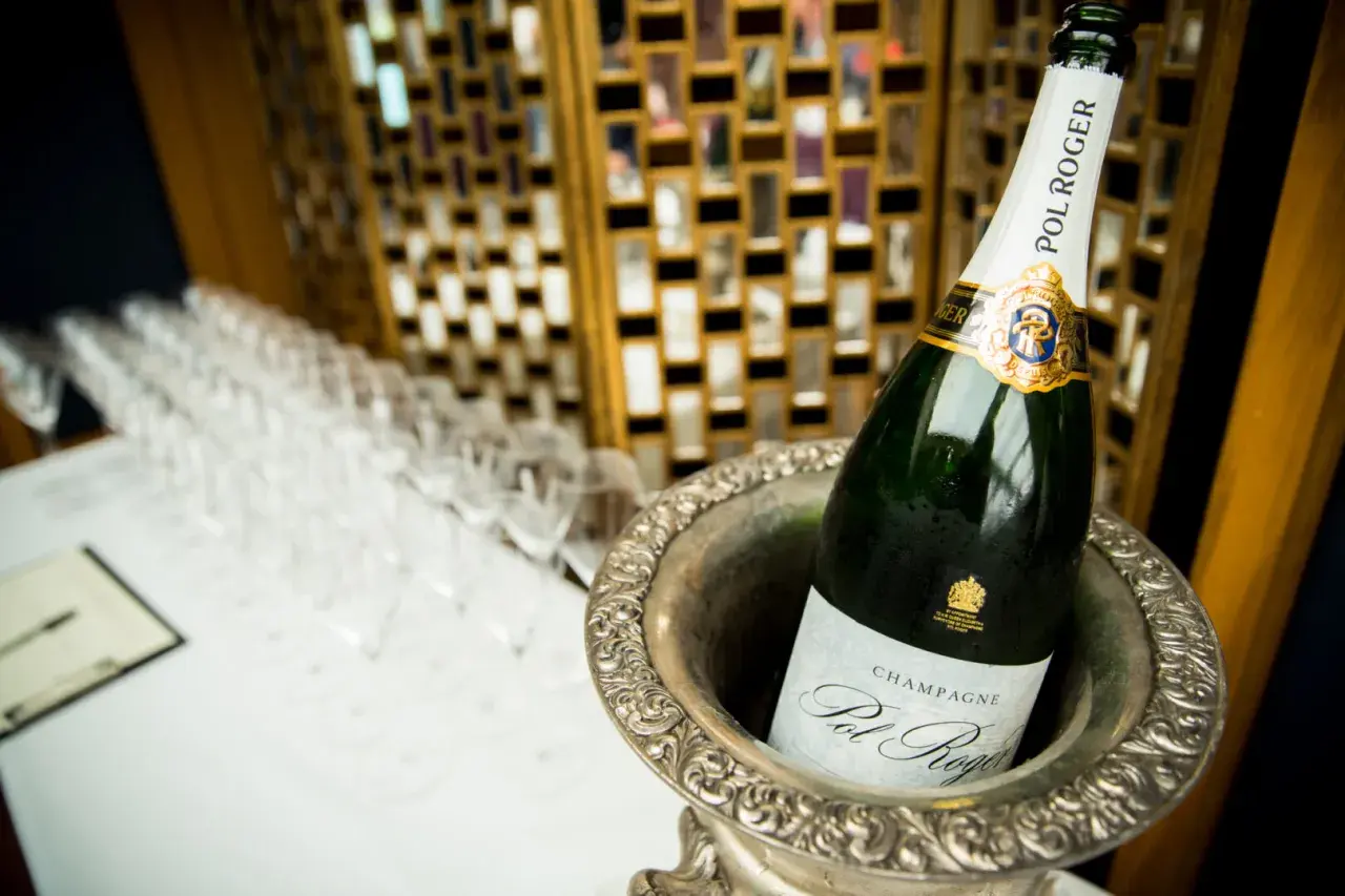 Bouteille de champagne Pol Roger dans un seau à glace, avec des flûtes alignées en arrière-plan.