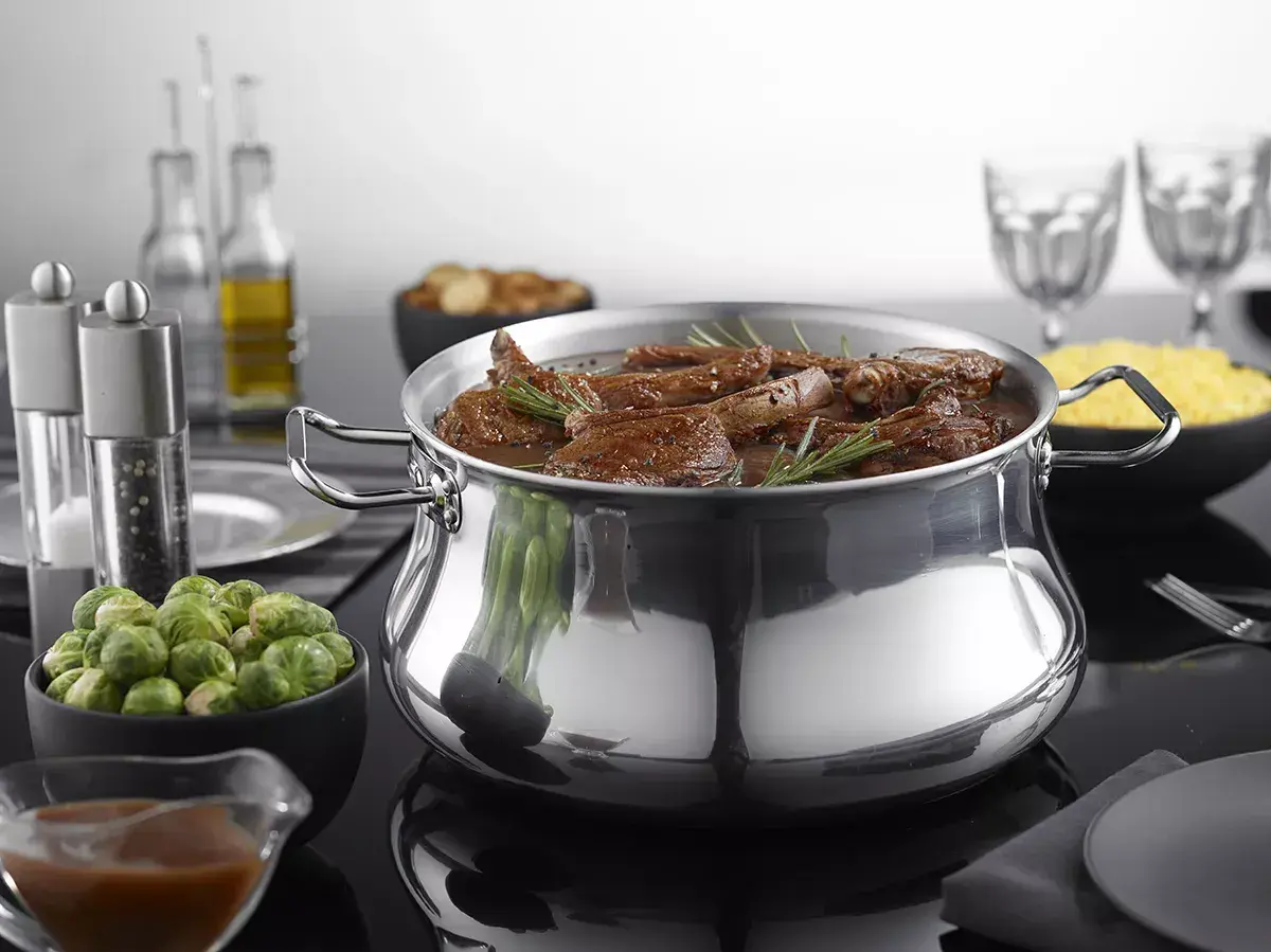 Un plat mijoté dans une cocotte en aluminium brillant, prêt pour le nettoyage. Des accompagnements comme des choux de Bruxelles et du riz sont disposés autour.