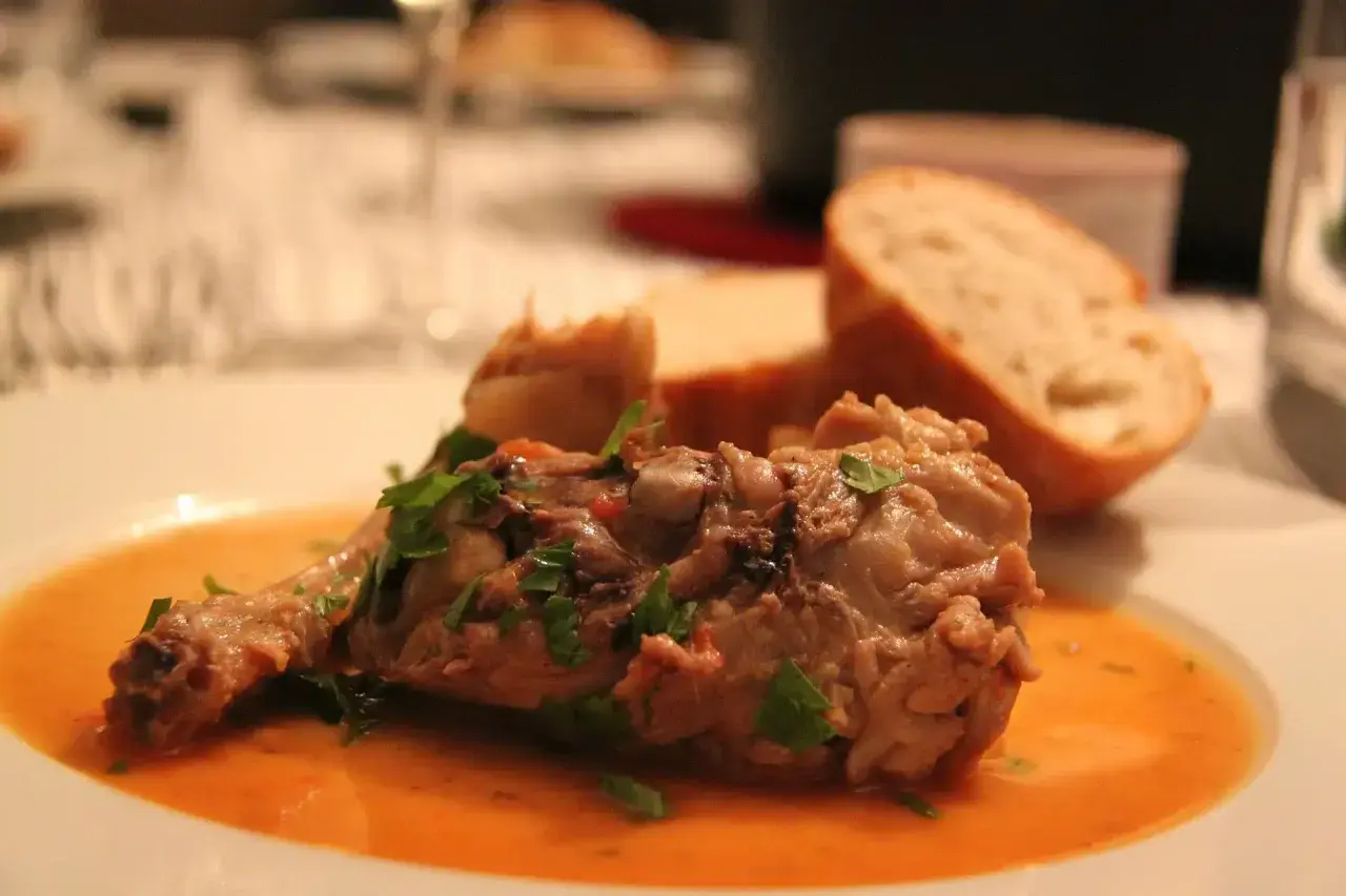 Un plat savoureux de viande mijotée, garni de persil frais, servi avec du pain. Parfait pour accompagner un osso bucco.