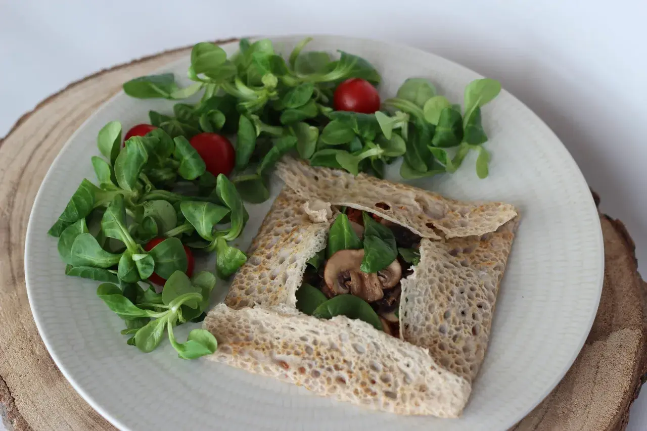 Une galette bretonne garnie de champignons et d'épinards, accompagnée d'une salade verte et de tomates cerises. Un délice pour accompagner un verre de vin.