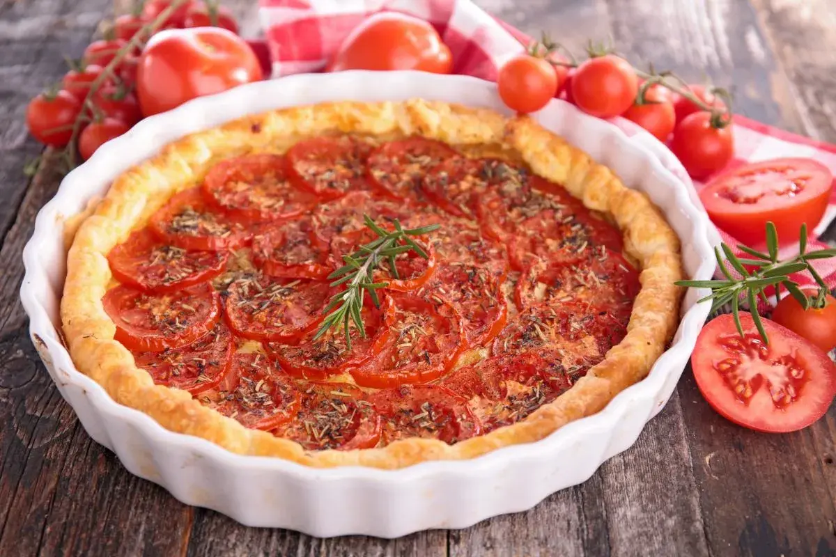Tarte aux tomates fraîches, garnie d'herbes et d'une branche de romarin. Un accompagnement tarte tomate parfait pour un repas d'été.