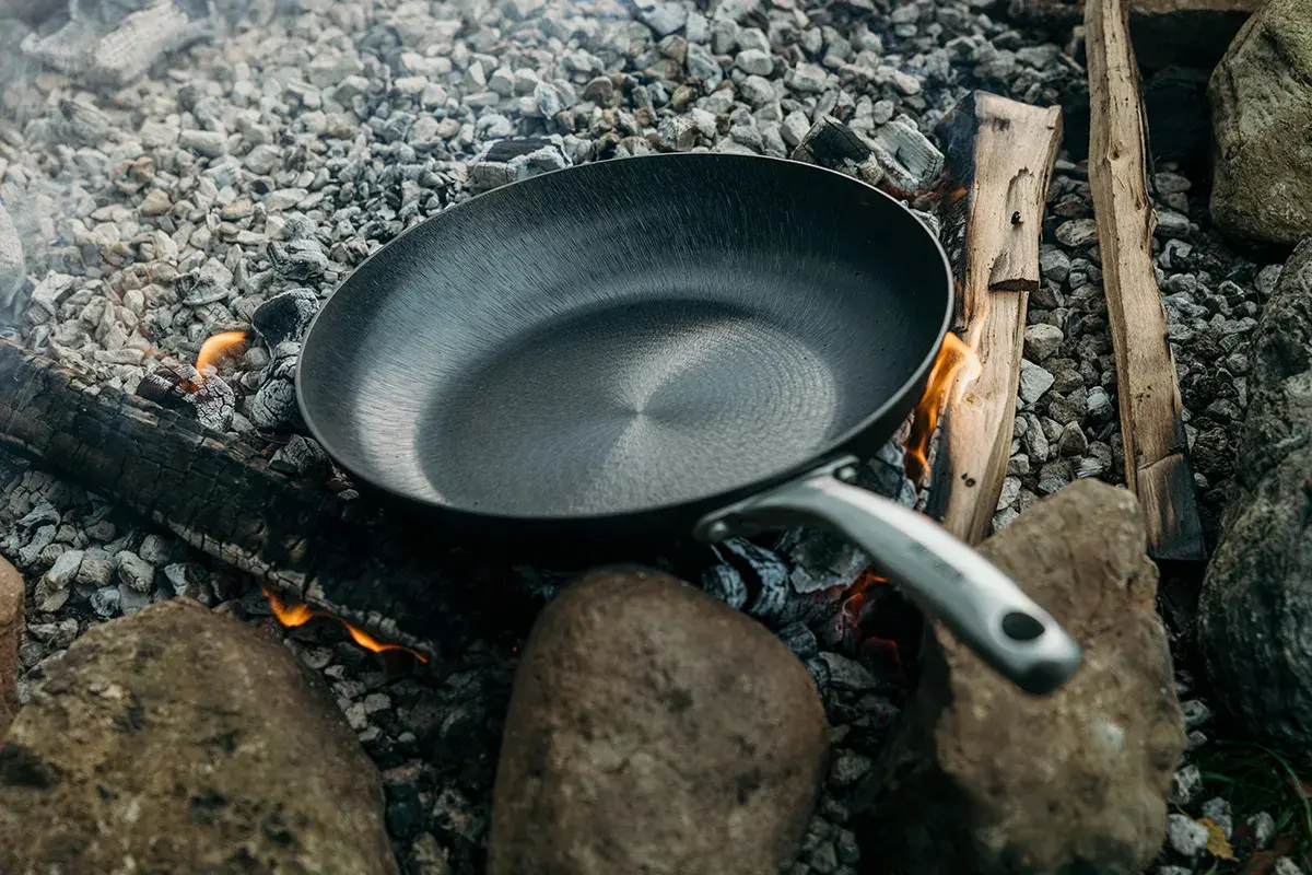 Poêle posée sur des braises et des pierres, prête à redresser le fond d'une poêle pour une cuisson en plein air.
