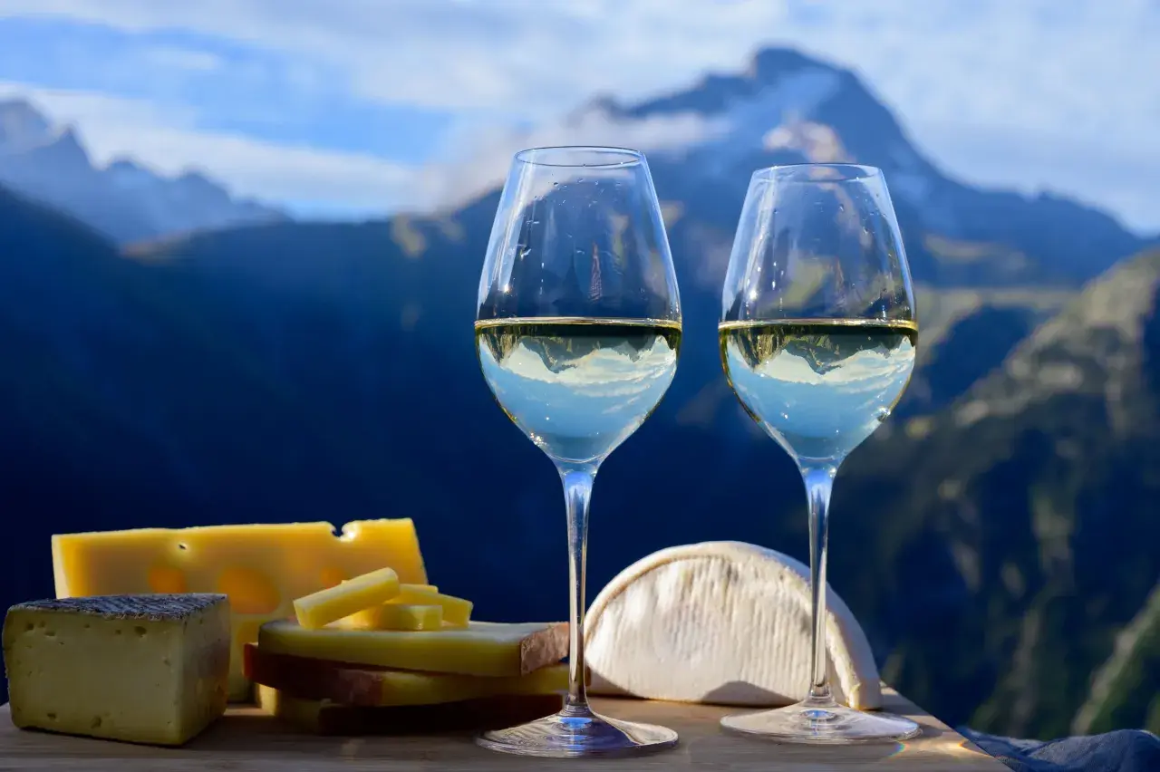 Deux verres de vin blanc avec des fromages devant des montagnes bleues.
