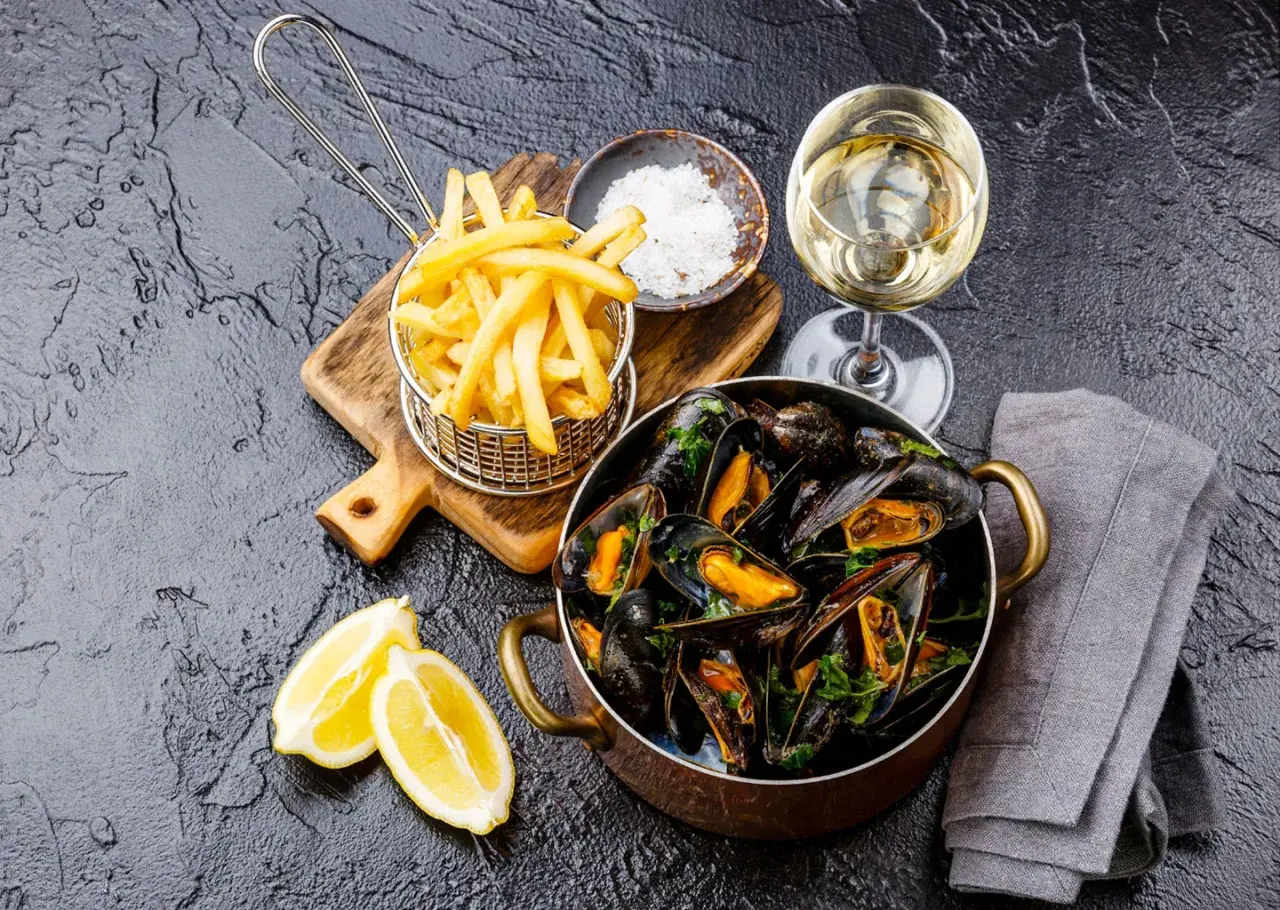 Un plat de moules frites, accompagné de quartiers de citron, d'une coupelle de gros sel et d'un verre de vin blanc.