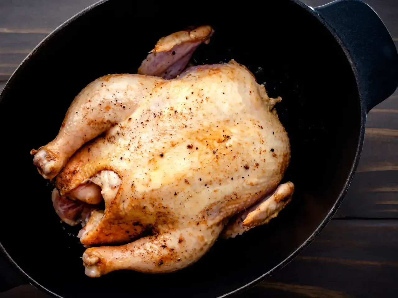 Un poulet rôti doré, assaisonné de poivre, repose dans une cocotte en fonte. Un délice prêt à être dégusté, un vrai poulet Calvi.