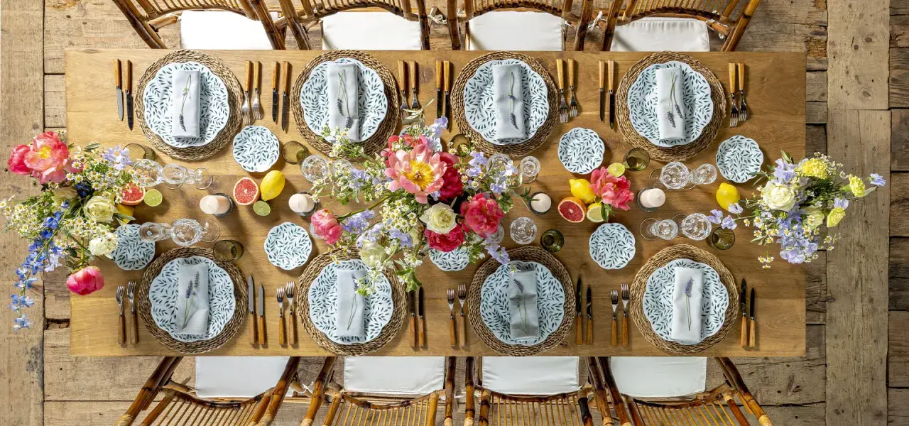 Table dressée pour un repas mariage champêtre, avec fleurs, fruits et vaisselle décorée de feuilles vertes.