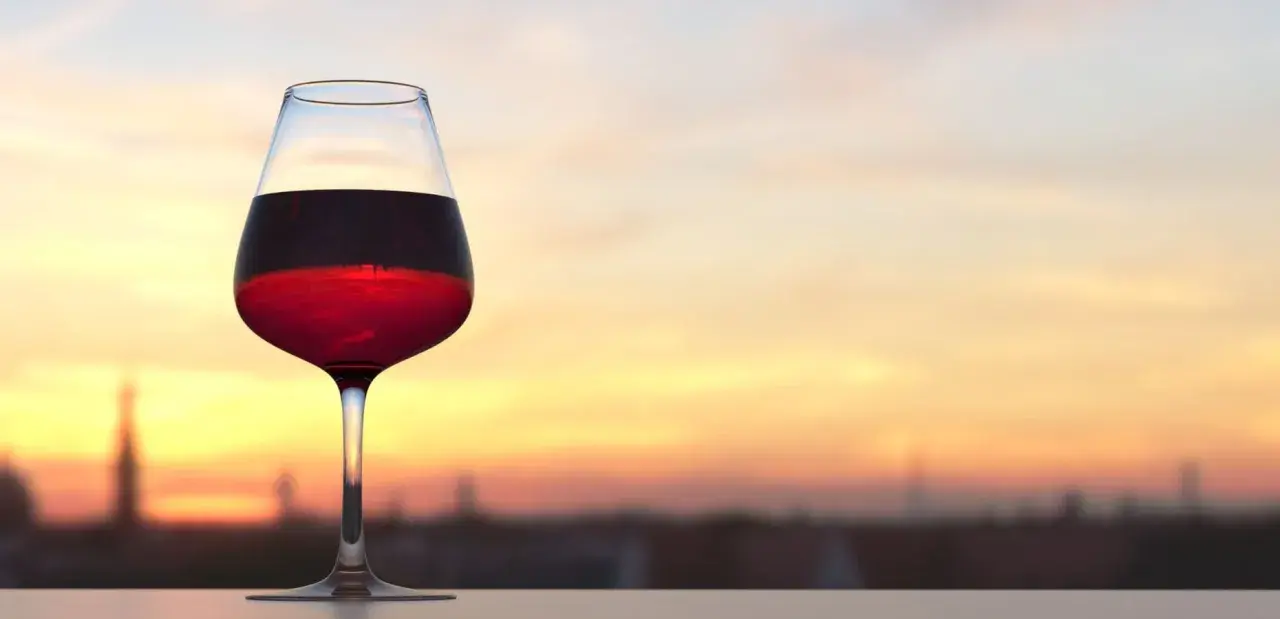 Verre de vin rouge bordeaux, parfait pour apprécier sa température idéale au coucher du soleil.