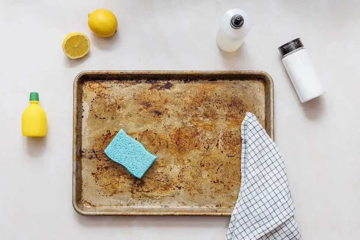Une plaque de cuisson en aluminium très sale, une éponge bleue, des citrons, une bouteille de produit vaisselle et une serviette à carreaux, prêts à décaper l'aluminium.