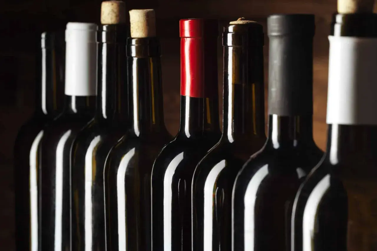 Une rangée de bouteilles de vin sombres, certaines avec des bouchons en liège, d'autres avec des capsules colorées. Un millésime Beaujolais pourrait se cacher parmi elles.