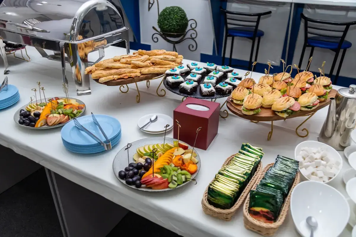 Un buffet de hors d'œuvre varié avec mini-burgers, pâtisseries, bâtonnets feuilletés et salade de fruits.