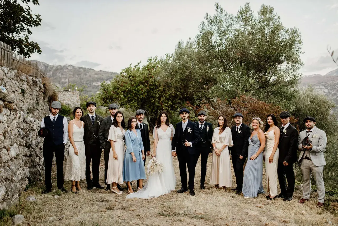 Mariage Peaky Blinders : le couple et leurs témoins, tous habillés de costumes d'époque, posent devant un paysage rocheux et verdoyant.