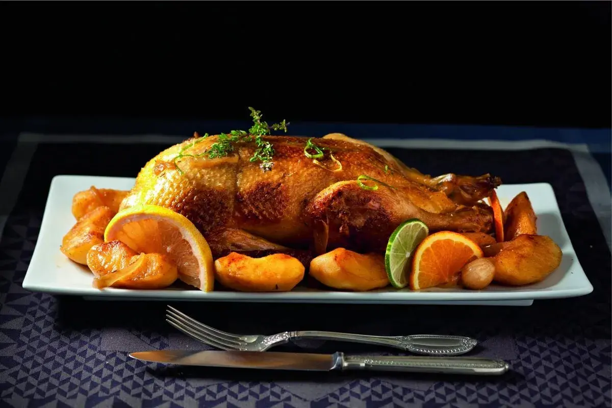 Canard rôti, pommes caramélisées et agrumes en accompagnement. Une canette dorée, prête à être dégustée.