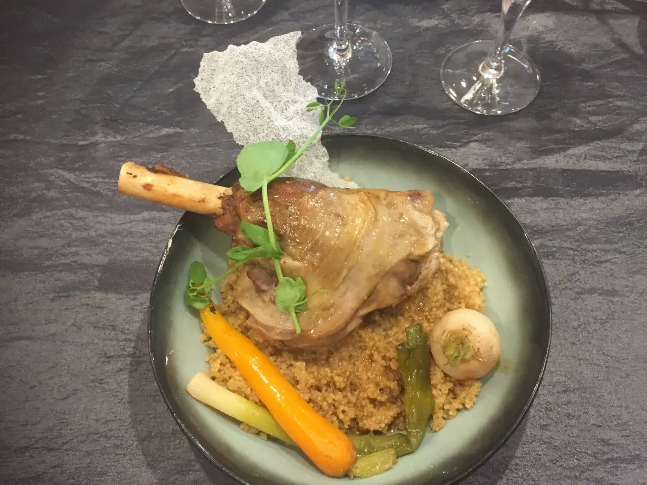 Souris d'agneau braisée au vin, servie sur un lit de couscous avec carottes et navet. Un plat savoureux et réconfortant.