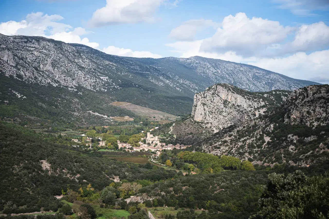 Vue panoramique sur le village de Saint-Guilhem-le-Désert, niché au creux de montagnes rocheuses. Un paysage idéal pour déguster un vin rouge local.