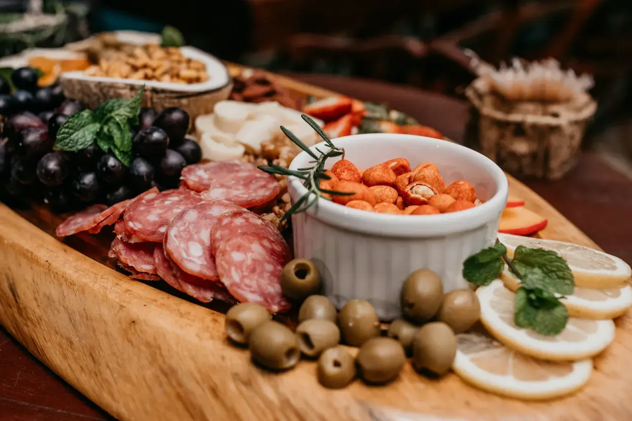 Un buffet campagnard pour 20 personnes : raisins noirs, salami, olives, cacahuètes épicées, citron et menthe sur un plateau en bois.