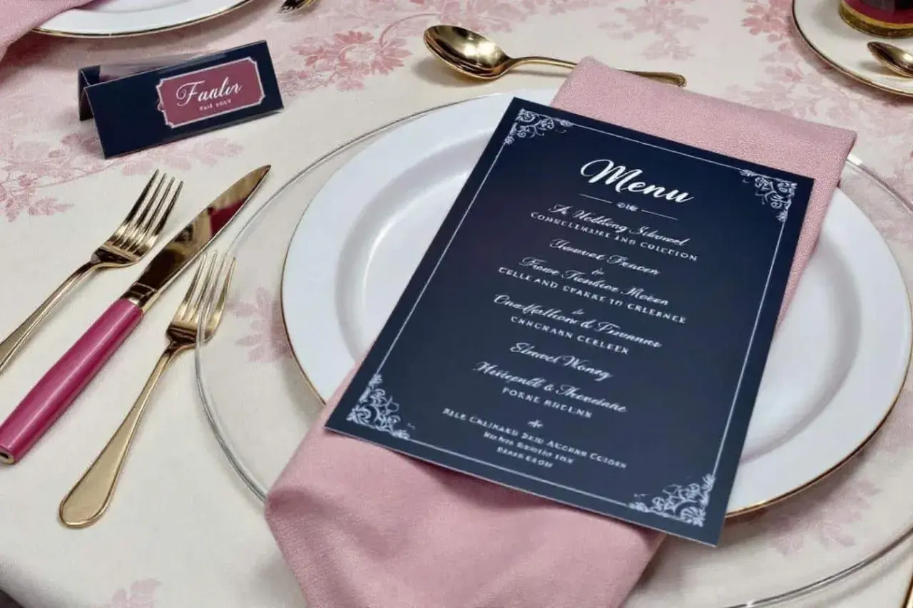 Une table dressée pour un mariage, avec un menu élégant proposant une idée menu mariage original. Couverts dorés, serviette rose poudré.