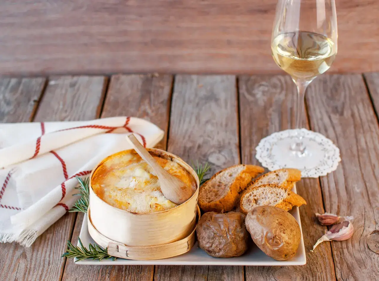 Un Mont d'Or au four, pommes de terre, pain et vin blanc. Quel vin avec Mont d'Or au four ? Un accord parfait pour un repas convivial.