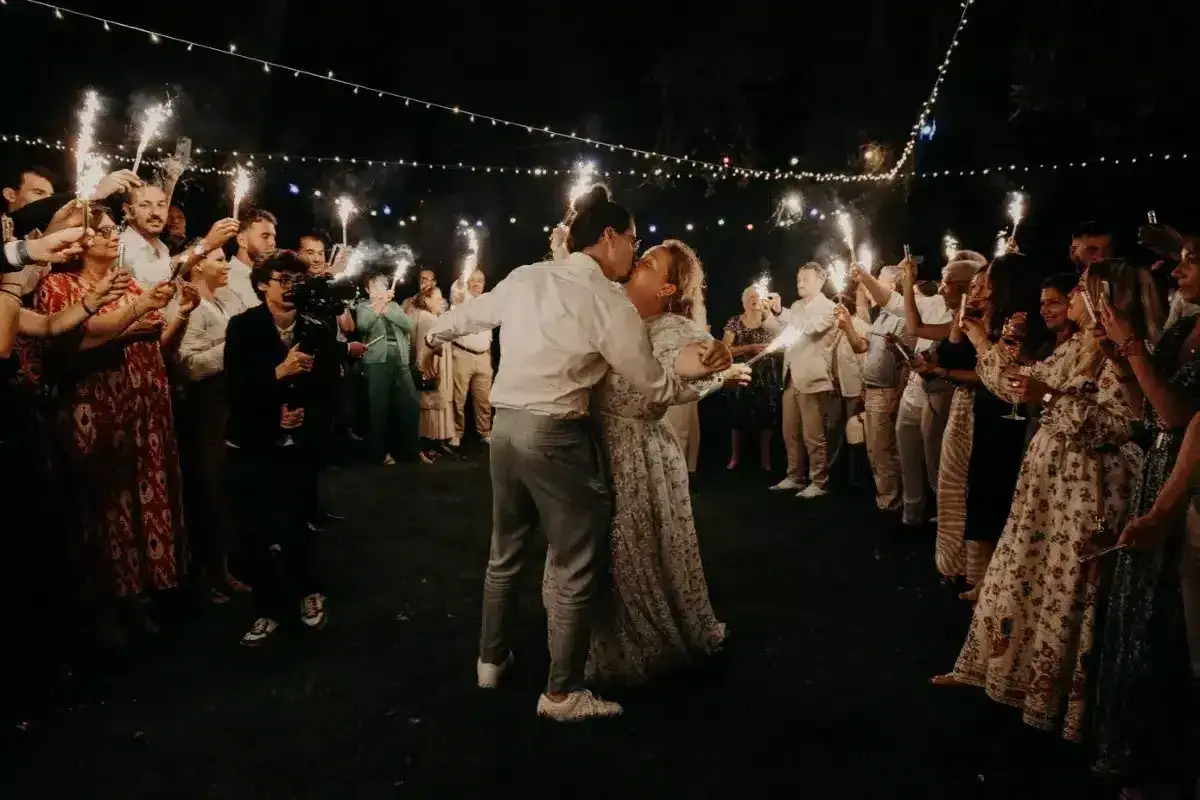 Mariage intime pour 30 personnes : le couple s'embrasse sous les feux de la rampe, entouré de ses proches.