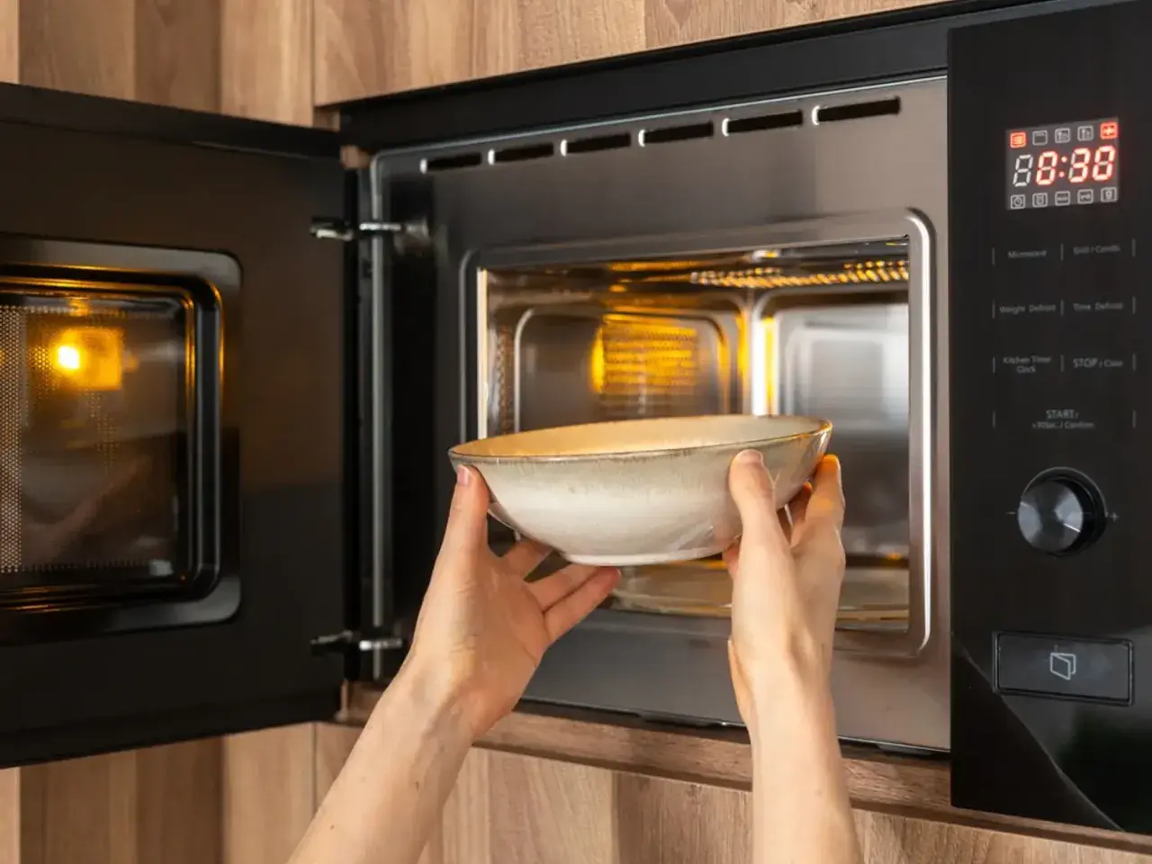 Une personne place une assiette dans un micro-ondes. La question "peut on mettre une assiette au micro-onde" est pertinente ici.