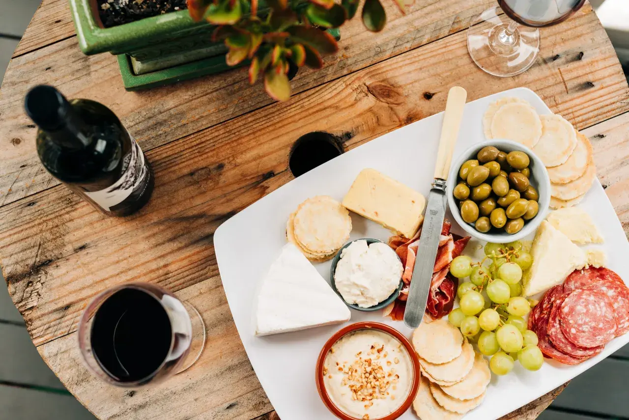 Un plateau de fromages variés, charcuterie, olives et raisins, accompagné d'une bouteille et d'un verre de vin rouge. Quel vin rouge avec un plateau de fromage varié ?