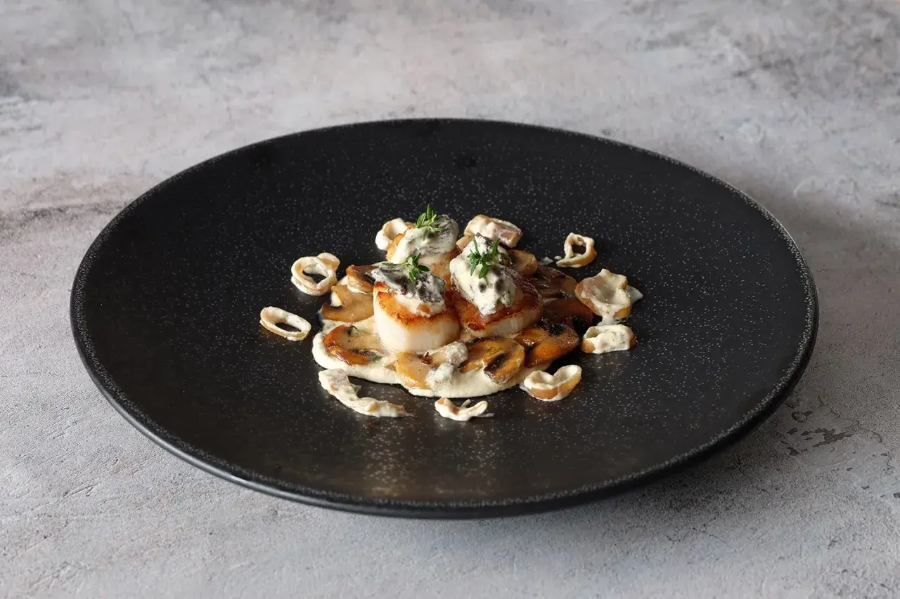 Coquilles Saint-Jacques aux morilles et leur sauce crémeuse au vin blanc, garnies de thym frais. Un délice visuel et gustatif.