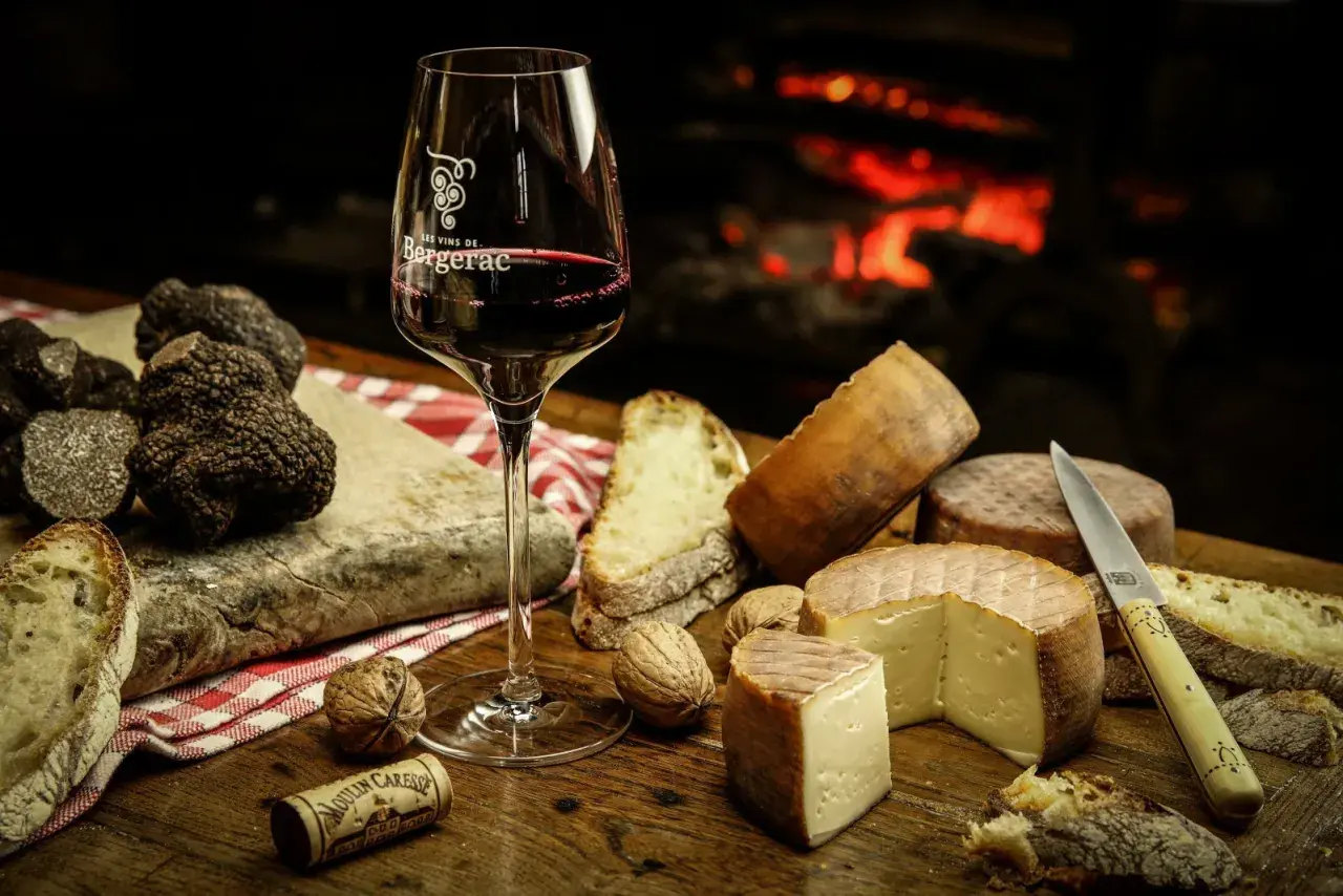 Verre de vin rouge, truffes noires, fromages et pain sur une table en bois, près d'une cheminée. Un délice pour accompagner un vin avec truffade.