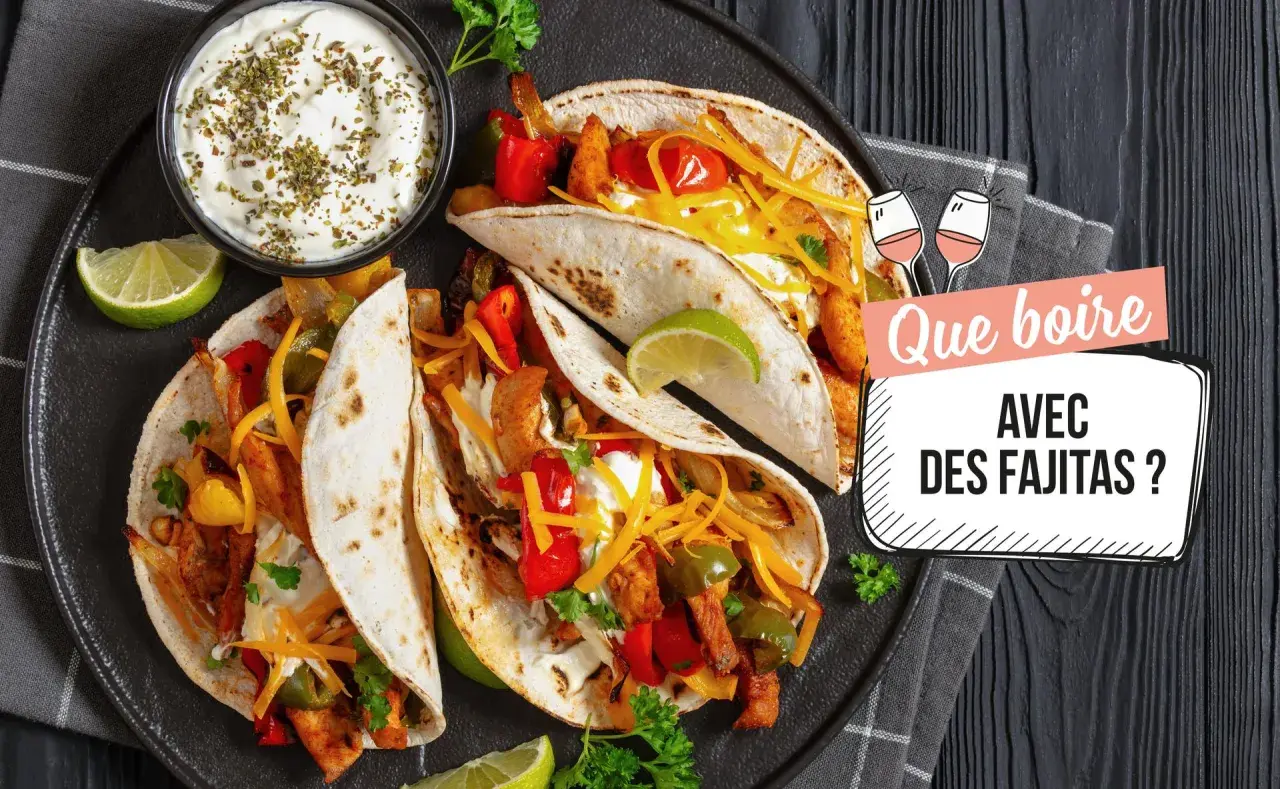 Assiette de fajitas savoureuses avec garnitures, crème aigre et quartiers de citron vert. Le texte demande "Que boire avec des fajitas ?".
