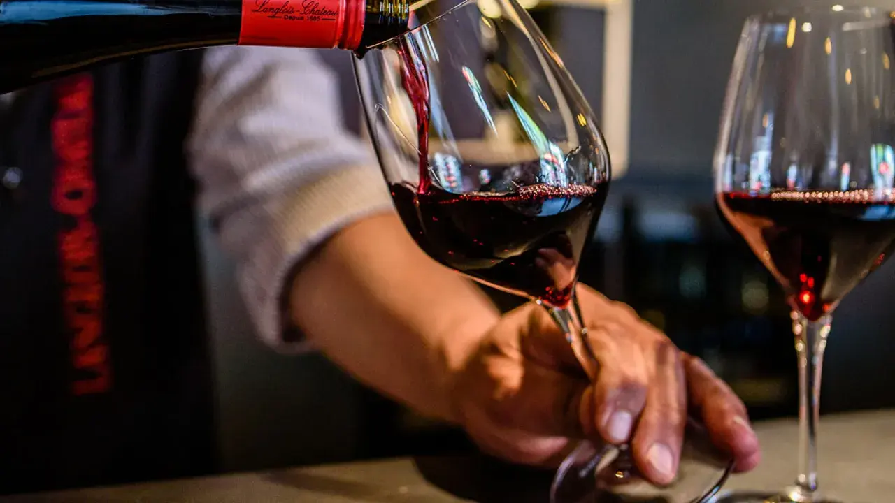 Service d'un vin rouge, idéalement servi à la bonne **température Saumur Champigny**. Le vin est versé dans un verre, avec une autre verre déjà rempli.