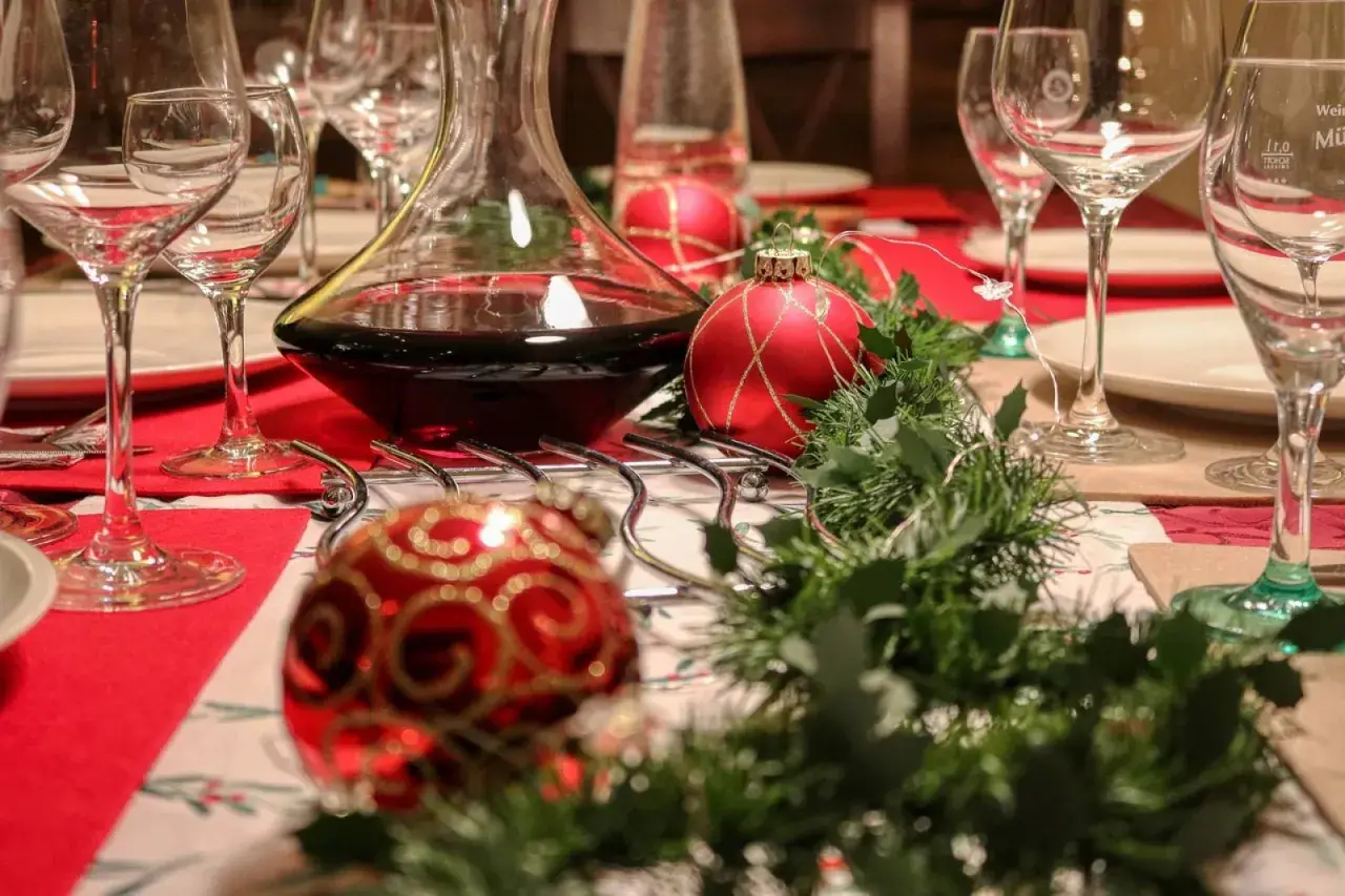 Table dressée pour Noël avec carafe de vin rouge. Combien de cubi de vin pour 40 personnes ? Boules rouges et guirlande verte.