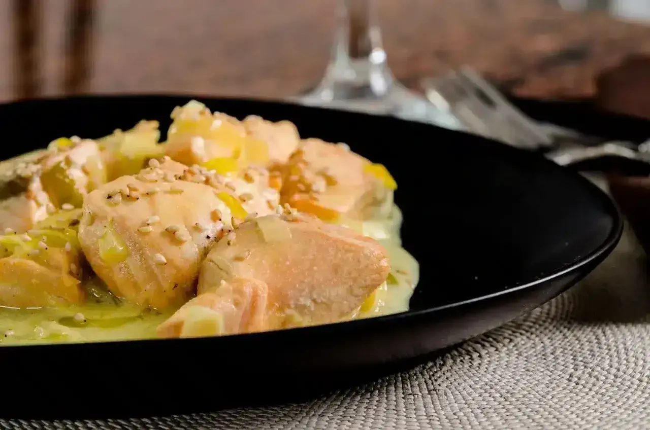 Délicieuse blanquette de saumon au vin blanc, parsemée de graines de sésame, servie dans une assiette noire.