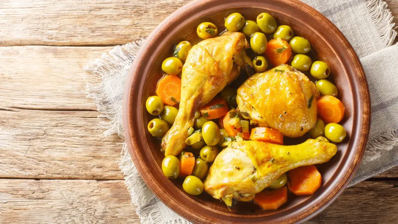 Un plat de tajine poulet citron avec des olives vertes et des carottes, servi dans un plat en terre cuite sur une table en bois.