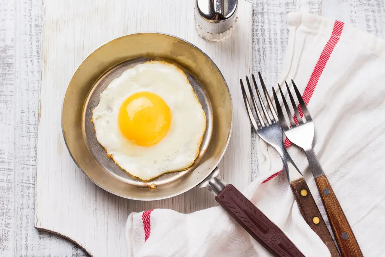 Un œuf au plat parfait, cuisiné dans une poêle inox, prêt à être dégusté avec deux fourchettes.