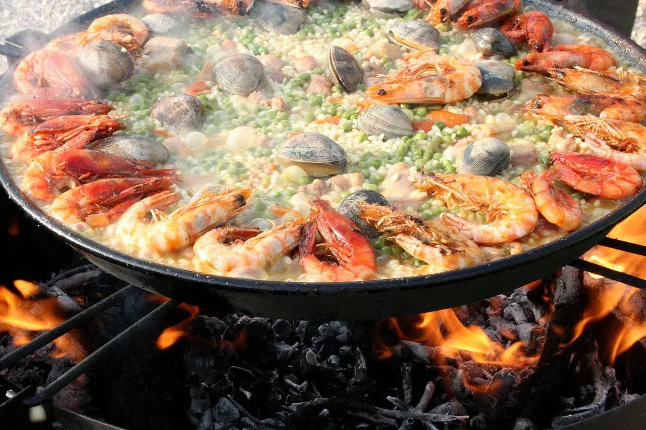 Gros plan sur une paella aux crevettes et palourdes, cuisant sur un feu de bois. Quel vin avec jambalaya ? Un blanc sec ou un rosé fruité serait parfait.