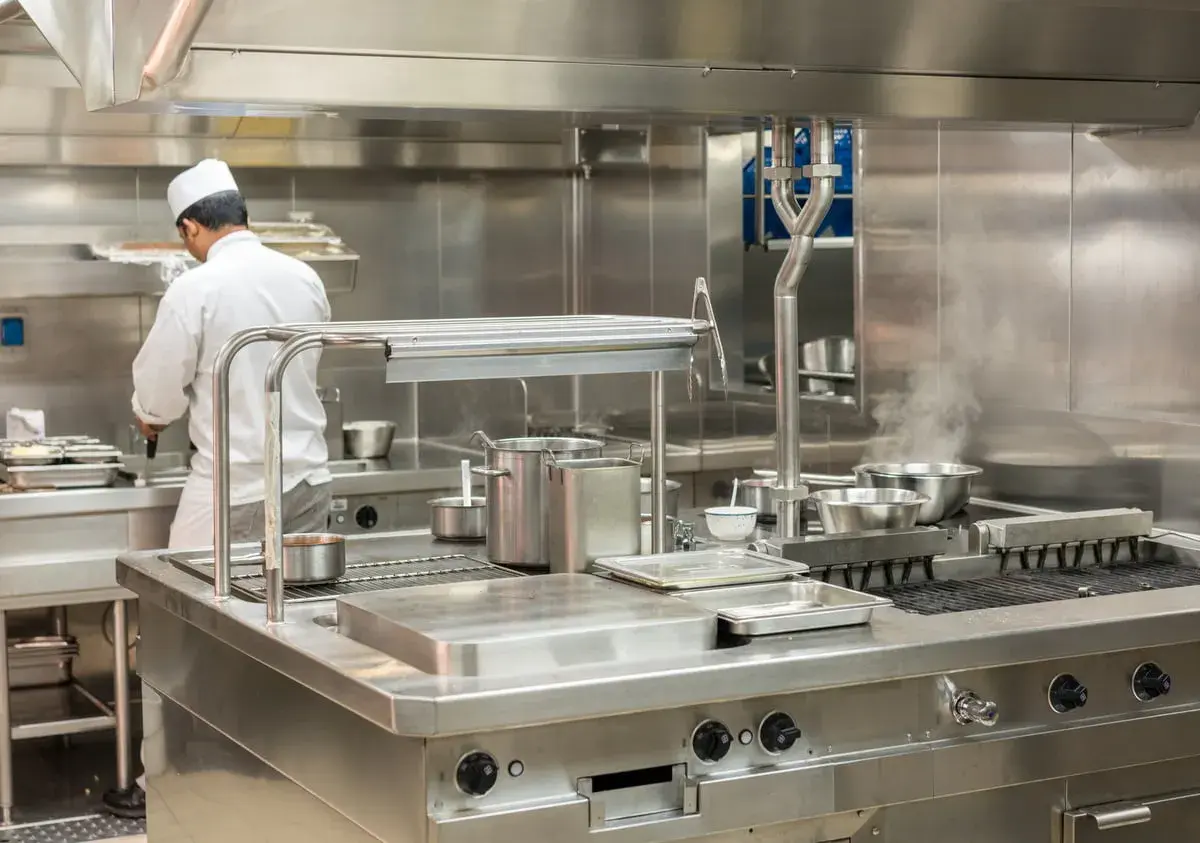 Un chef travaille dans une cuisine professionnelle étincelante, tout en acier inoxydable, le meilleur inox pour une hygiène parfaite.