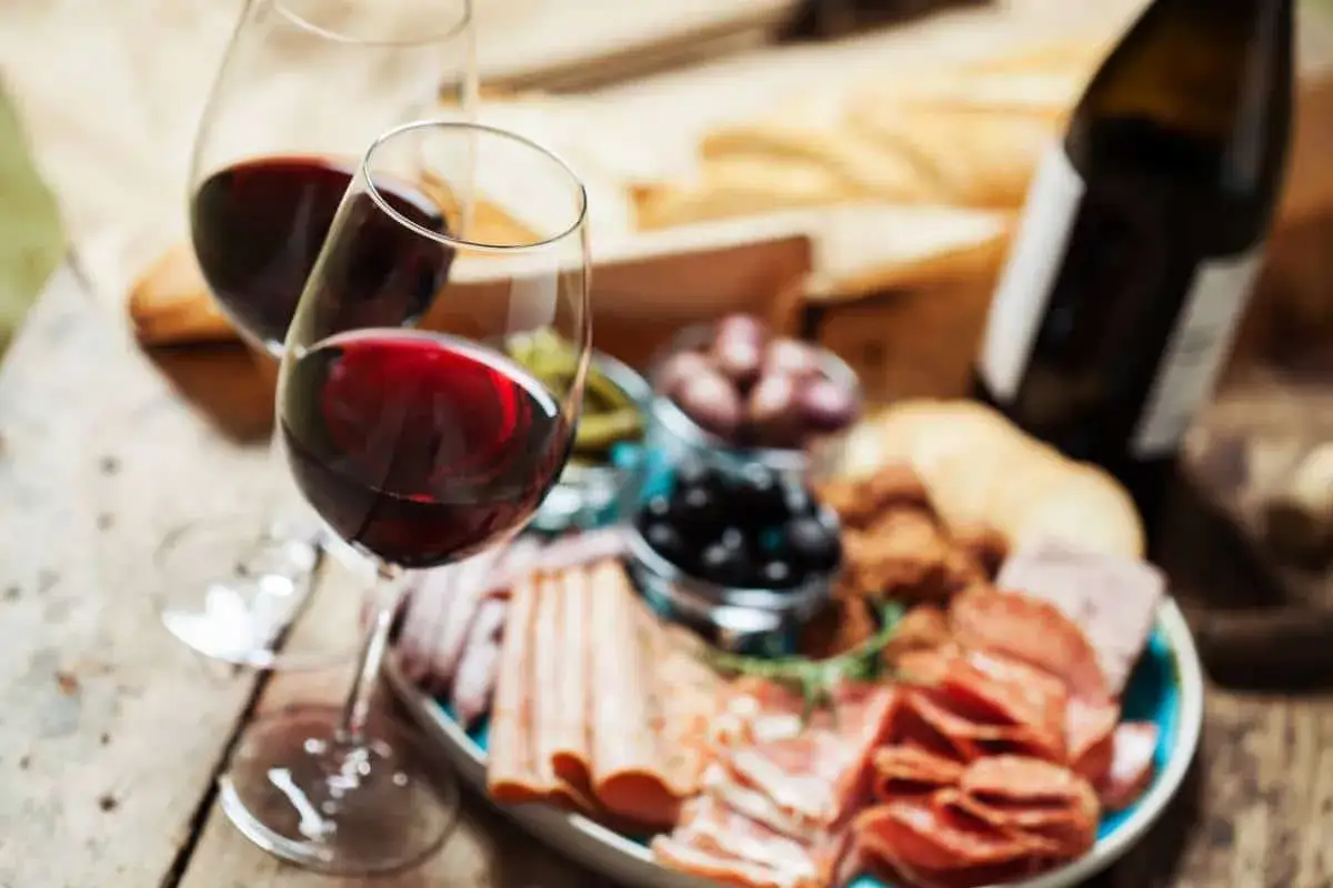 Deux verres de vin rouge parfaits pour accompagner un buffet froid avec charcuterie, olives et pain.