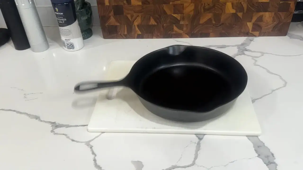 Po&ecirc;le en fonte noire sur une planche &agrave; d&eacute;couper blanche, pr&ecirc;te &agrave; redresser le fond.