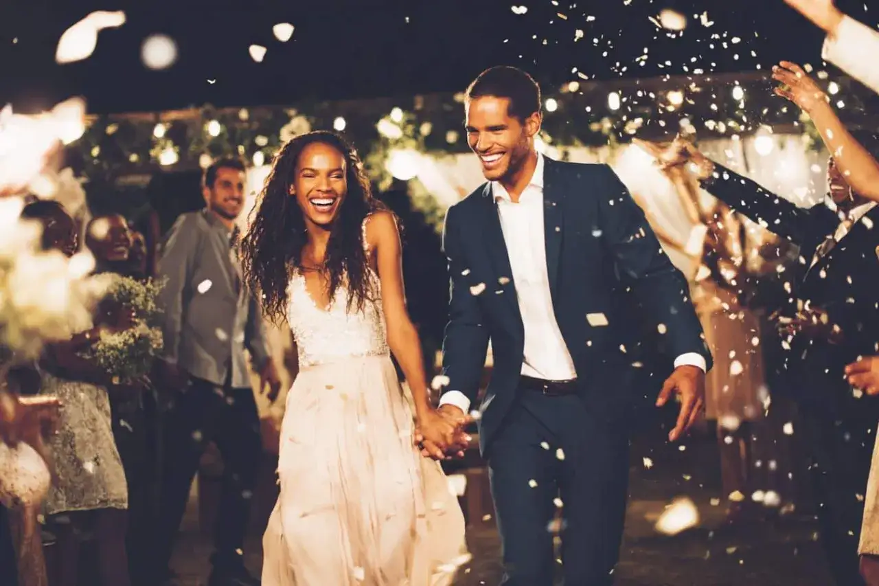 Un couple heureux, tout juste mari&eacute;, traverse une haie d'honneur sous une pluie de p&eacute;tales. Ils semblent r&eacute;pondre &agrave; un questionnaire pour les futurs mari&eacute;s, rempli de joie.