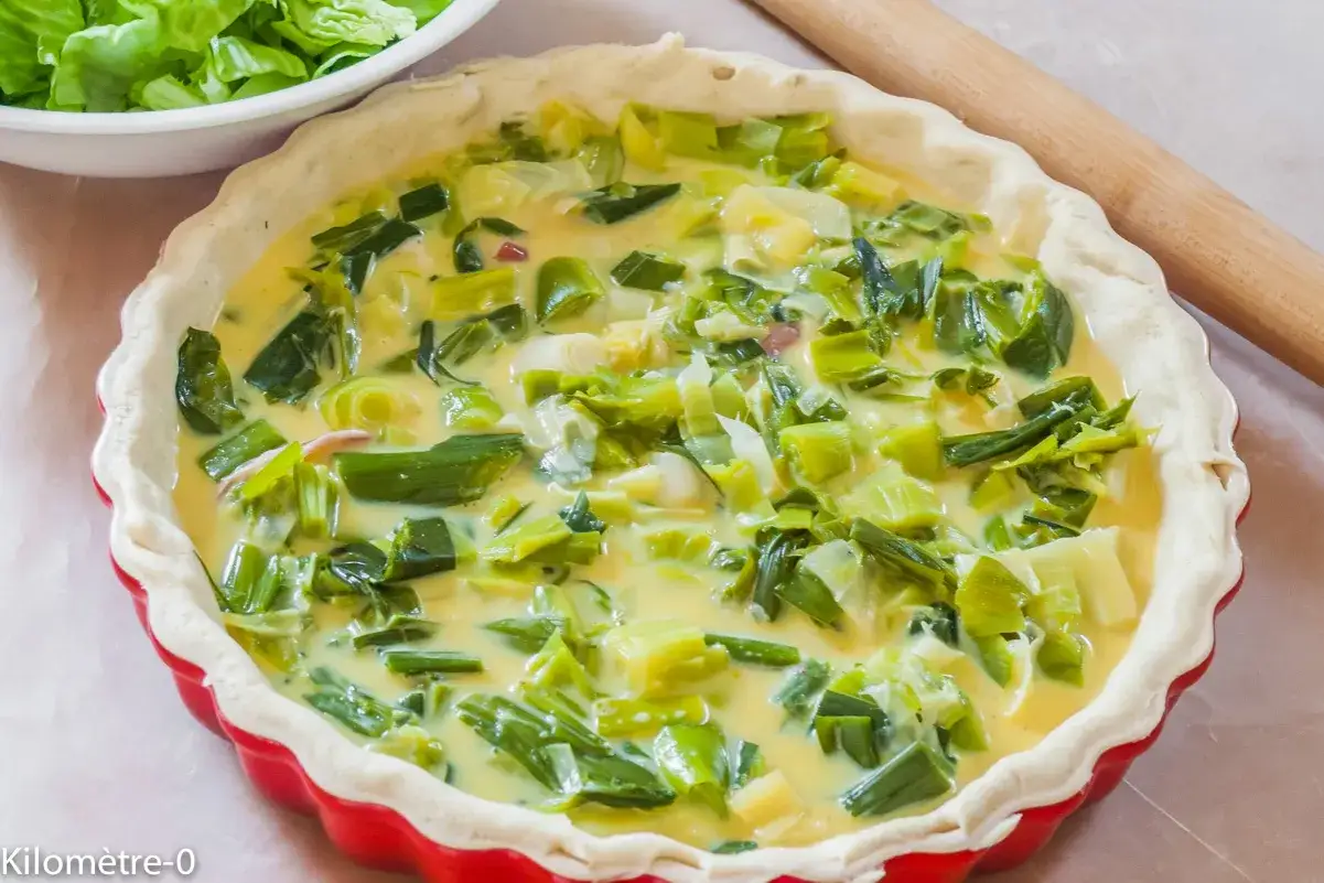 Tarte aux poireaux crue dans un moule rouge, pr&ecirc;te &agrave; cuire. Un accompagnement parfait pour un repas l&eacute;ger.