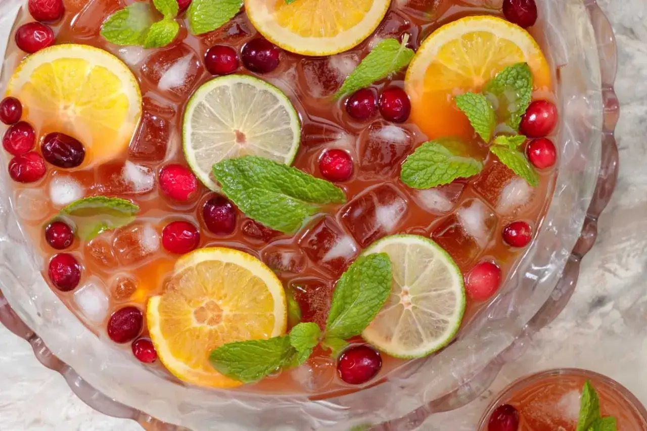 Un grand bol de punch fruité avec des tranches d'orange, de citron vert, des canneberges et de la menthe. 5 litres de punch pour combien de personnes ? Idéal pour une fête !