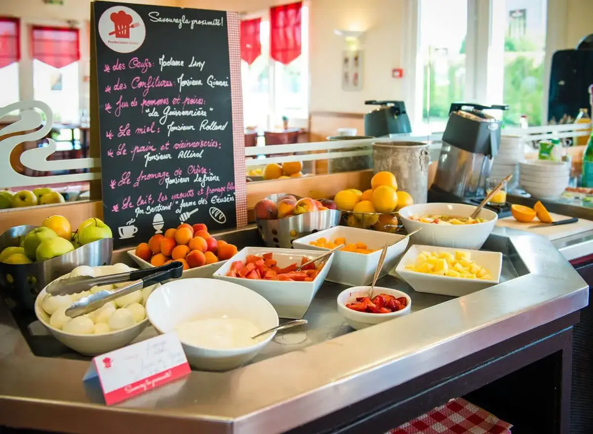 Un buffet de repas du matin avec des fruits frais, des &oelig;ufs, du fromage et des confitures. Une ardoise liste les produits locaux.